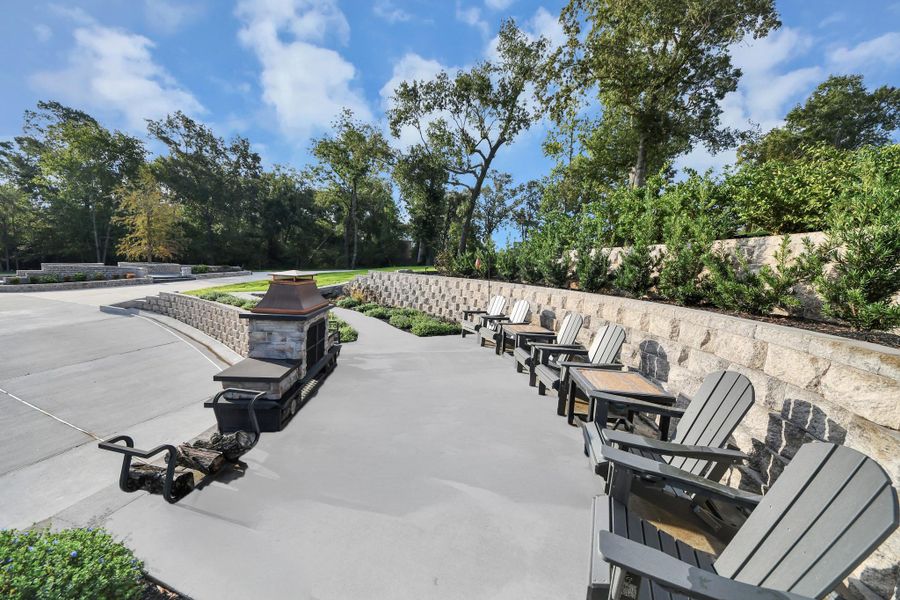 Spacious outdoor patio featuring a charming stone fireplace, perfect for gatherings, surrounded by lush greenery and comfortable seating.