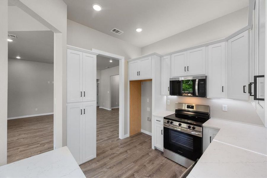Modern kitchen featuring white shaker cabinetry, stainless steel range and microwave, white countertops, and wood-finish flooring