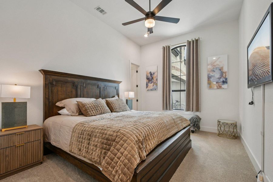 This room features a dark wood bed frame and nightstand, neutral carpet, and a ceiling fan with integrated lighting This room features a dark wood bed frame and nightstand, neutral carpet, and a ceiling fan with integrated lighting