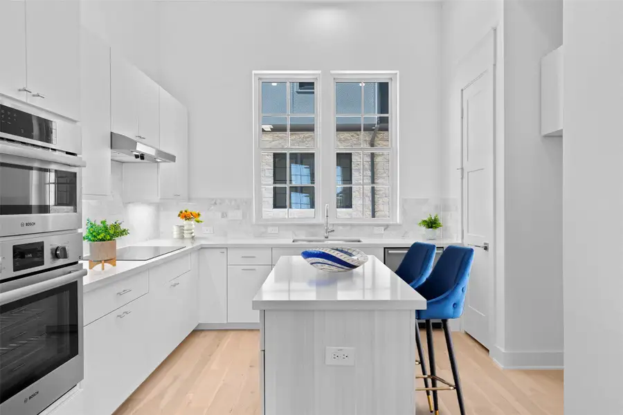 Kitchen with white cabinets, light wood finished floors, a center island, stainless steel double oven, and a kitchen breakfast bar