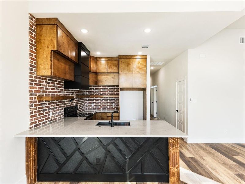 Kitchen with a peninsula, light stone counters, backsplash, black / electric stove, and light wood-style flooring Kitchen with a peninsula, light stone counters, backsplash, black / electric stove, and light wood-style flooring