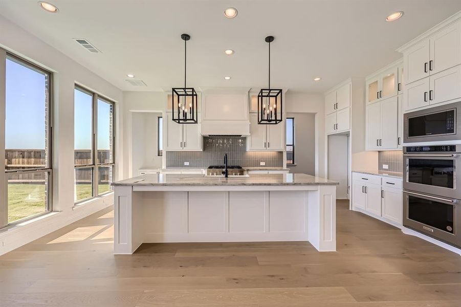 Kitchen featuring an island with sink, a wealth of natural light, white cabinetry, and light hardwood / wood-style flooring