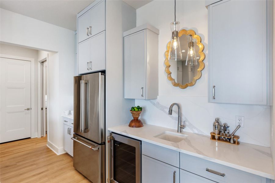 Kitchen featuring beverage cooler, high end fridge, light wood finished floors, hanging light fixtures, and decorative backsplash Kitchen featuring beverage cooler, high end fridge, light wood finished floors, hanging light fixtures, and decorative backsplash