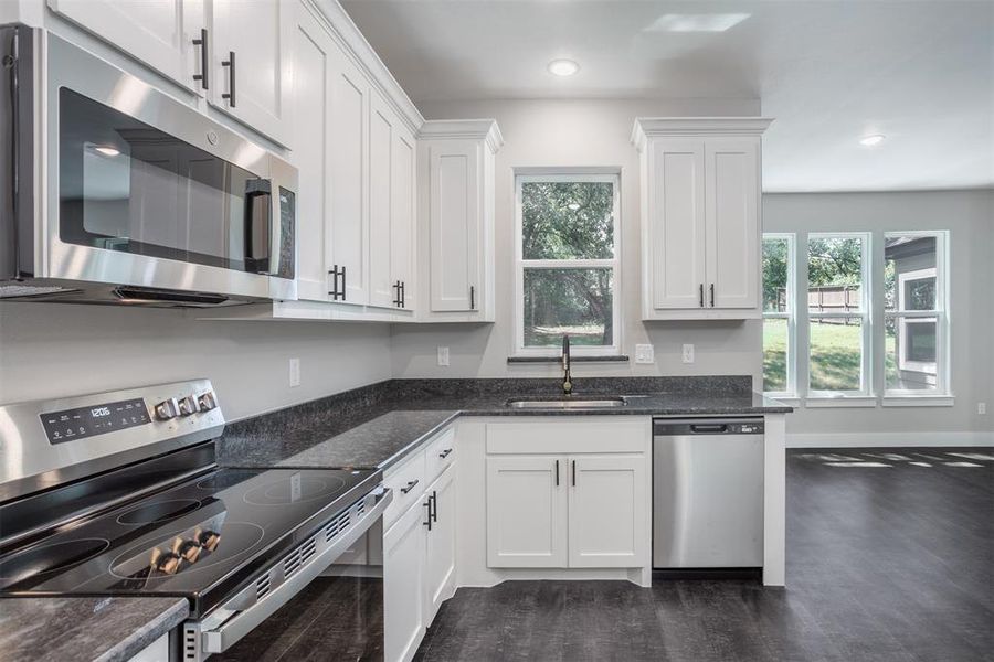 Kitchen featuring appliances with stainless steel finishes, dark stone countertops, white cabinetry, dark wood-style floors, and recessed lighting Kitchen featuring appliances with stainless steel finishes, dark stone countertops, white cabinetry, dark wood-style floors, and recessed lighting