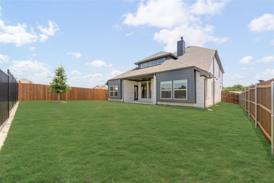 Rear view of two-story home with brick and gray siding, covered patio, and large fenced backyard with green lawn. Rear view of two-story home with brick and gray siding, covered patio, and large fenced backyard with green lawn.