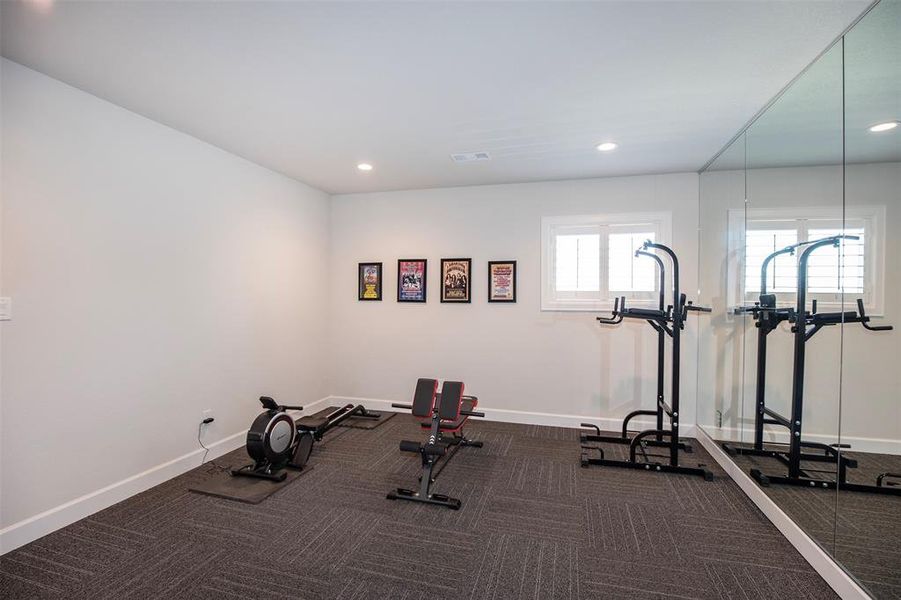 This home features a bright, well-lit fitness room with modern equipment, carpeted flooring, and a large mirrored wall, perfect for workouts.