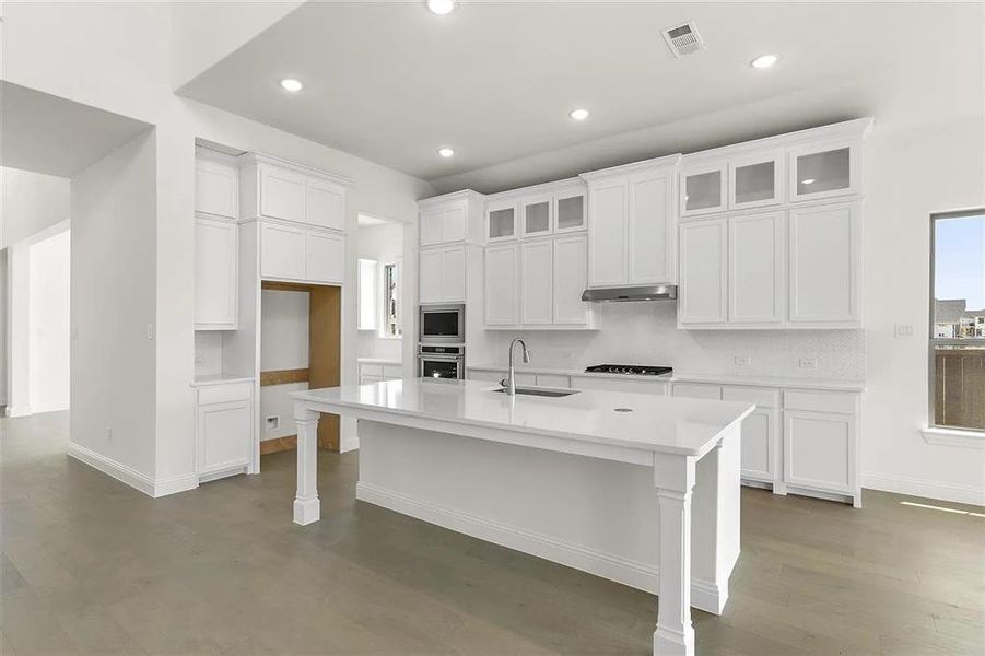 Kitchen featuring white cabinets, sink, an island with sink, and built in microwave