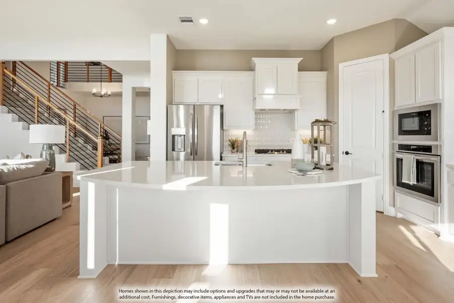 Open kitchen with curved white island, white cabinets, stainless appliances, and light wood floors