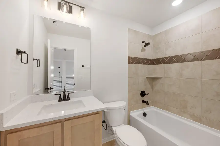 Bathroom with quartz vanity, wood cabinets, and tiled tub-shower combo with decorative accent border