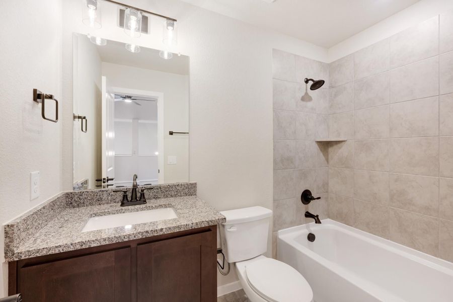 Bathroom with granite vanity, dark wood cabinets, and tiled shower-tub combo with oil-rubbed bronze fixtures