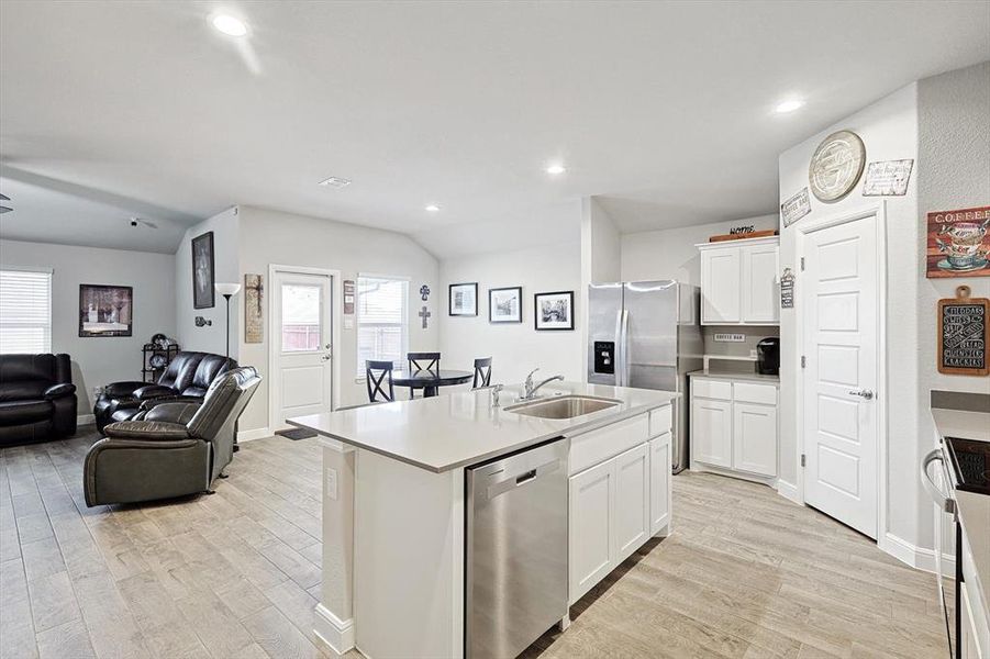 Kitchen featuring a center island with sink, stainless steel appliances, open floor plan, white cabinets, and a sink
