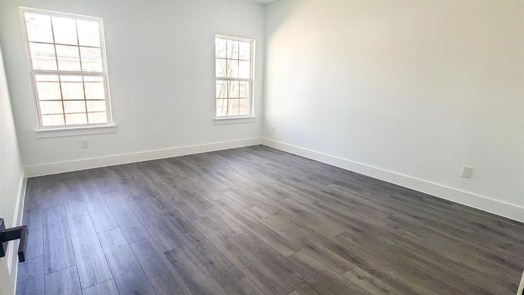 Room featuring wood-finish flooring, white baseboards, and two windows with white trim Room featuring wood-finish flooring, white baseboards, and two windows with white trim