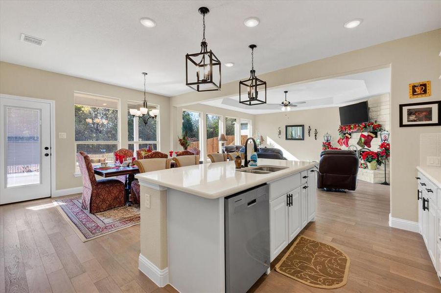 Kitchen with white cabinets, an island with sink, dishwasher, and hanging light fixtures Kitchen with white cabinets, an island with sink, dishwasher, and hanging light fixtures