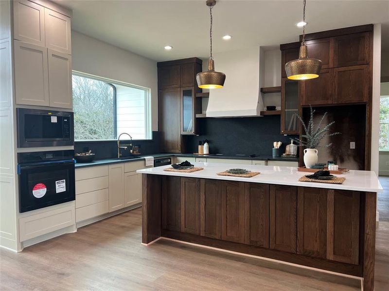 Kitchen with pendant lighting, dark brown cabinets, custom range hood, built in microwave, and oven