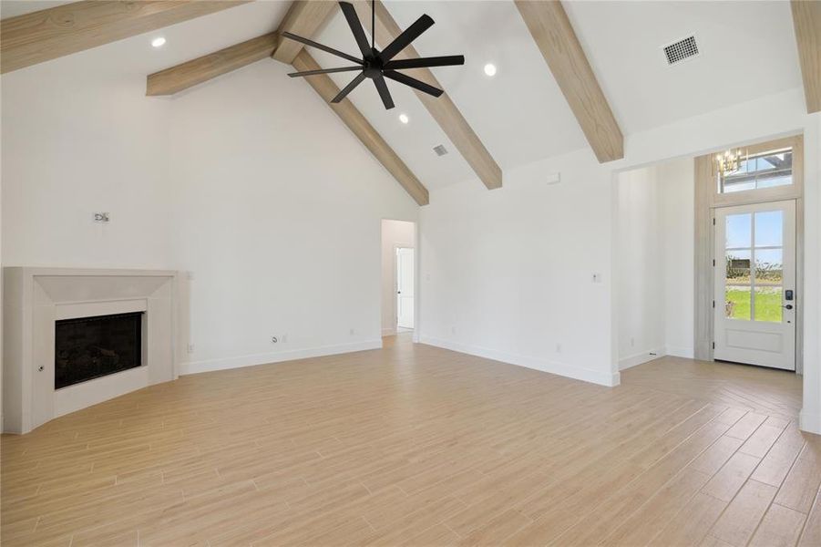 Unfurnished living room with ceiling fan with notable chandelier, beam ceiling, light wood-type flooring, and high vaulted ceiling