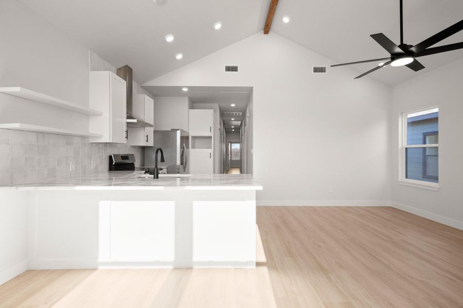 Kitchen featuring white cabinets, open shelves, light stone countertops, a peninsula, and light wood-style flooring