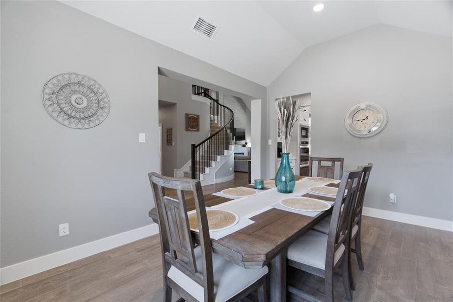 Spacious dining area featuring vaulted ceilings, recessed lighting, wood-finish flooring, and an open entryway to the main staircase