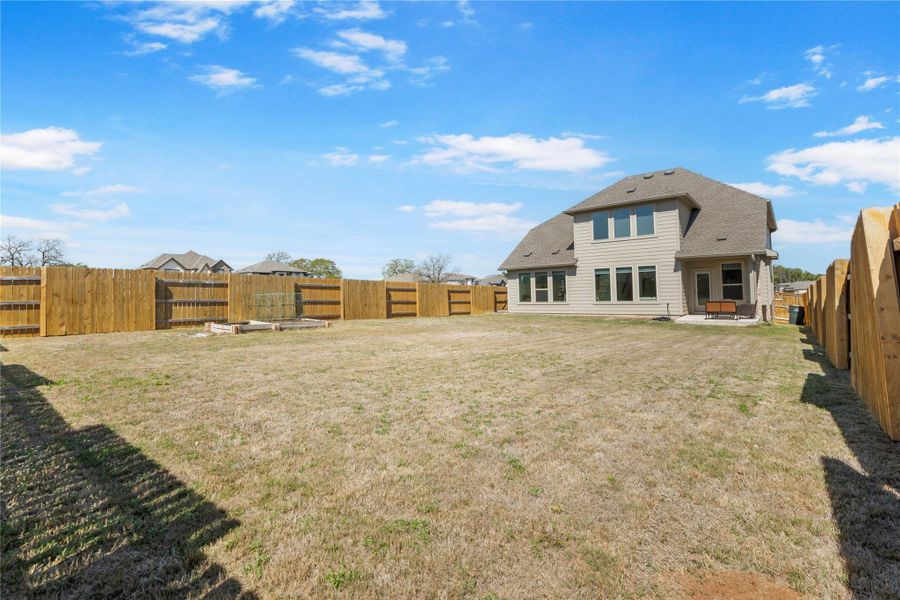 A spacious backyard with a private wood fence encloses a home featuring multiple large windows and an outdoor seating area. A spacious backyard with a private wood fence encloses a home featuring multiple large windows and an outdoor seating area.