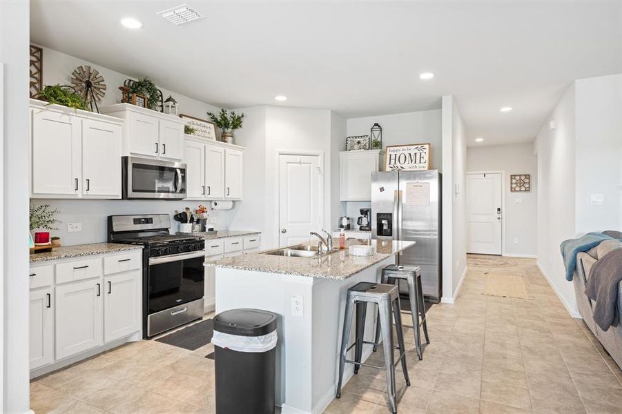 Kitchen with stainless steel appliances, light stone countertops, a center island with sink, white cabinets, and recessed lighting