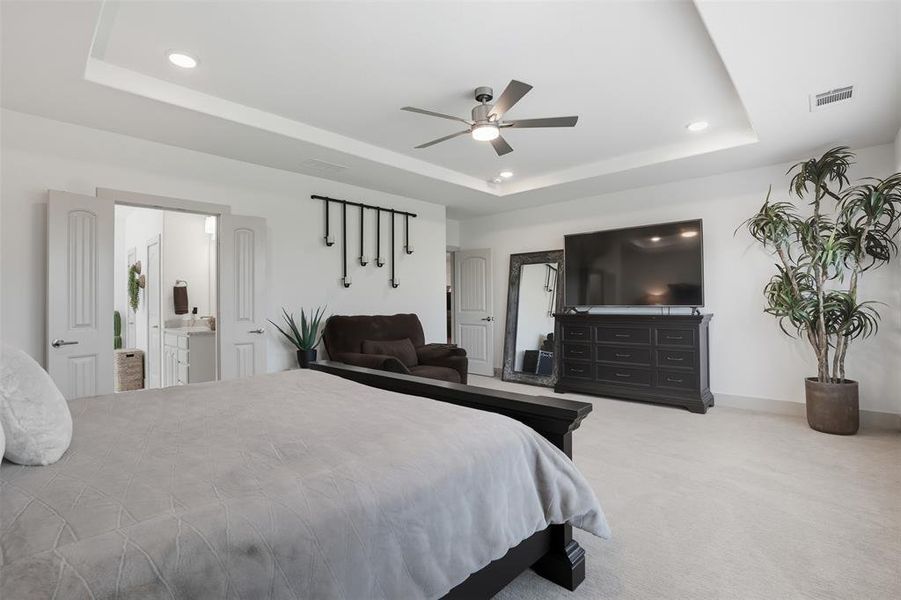 Bedroom featuring a raised ceiling, light carpet, a ceiling fan, recessed lighting, and ensuite bath Bedroom featuring a raised ceiling, light carpet, a ceiling fan, recessed lighting, and ensuite bath