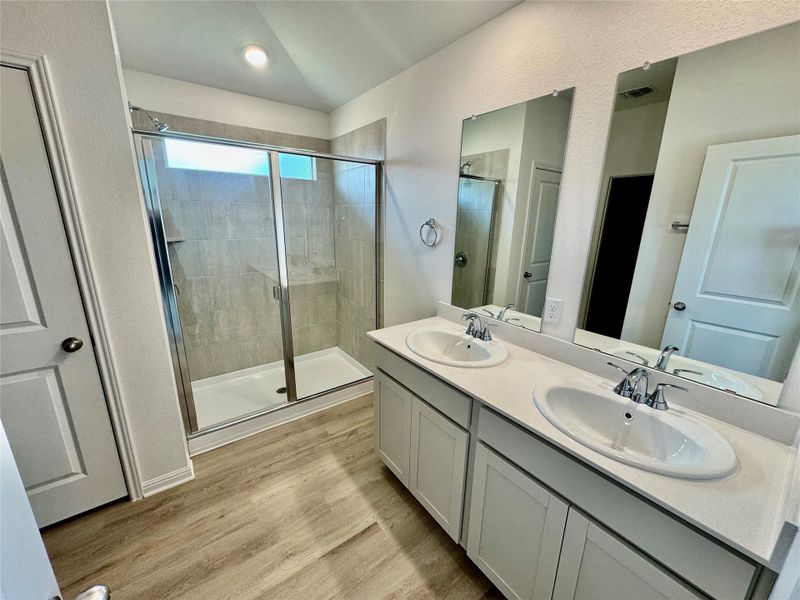 Bathroom with a stall shower, double vanity, light wood-style flooring, and a textured wall Bathroom with a stall shower, double vanity, light wood-style flooring, and a textured wall