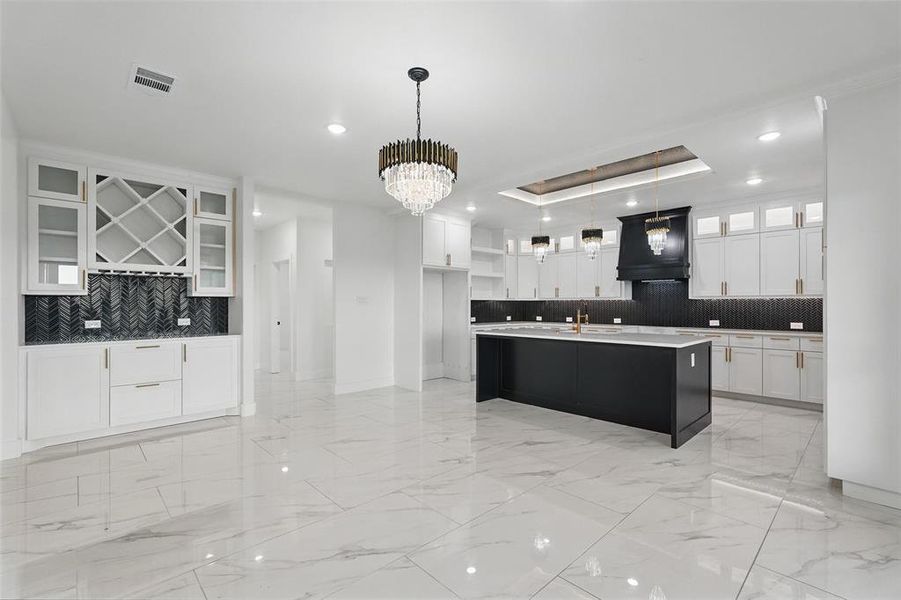 Kitchen with custom range hood, decorative backsplash, light marble finish floors, a sink, and white cabinets Kitchen with custom range hood, decorative backsplash, light marble finish floors, a sink, and white cabinets