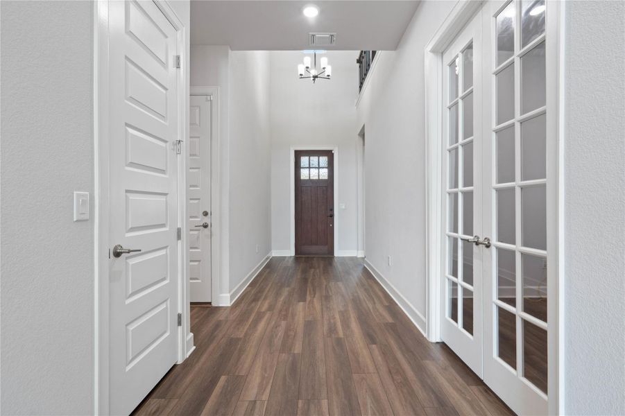 Rich wood-look flooring guides visitors through a soaring foyer flanked by classic glass-paneled doors.