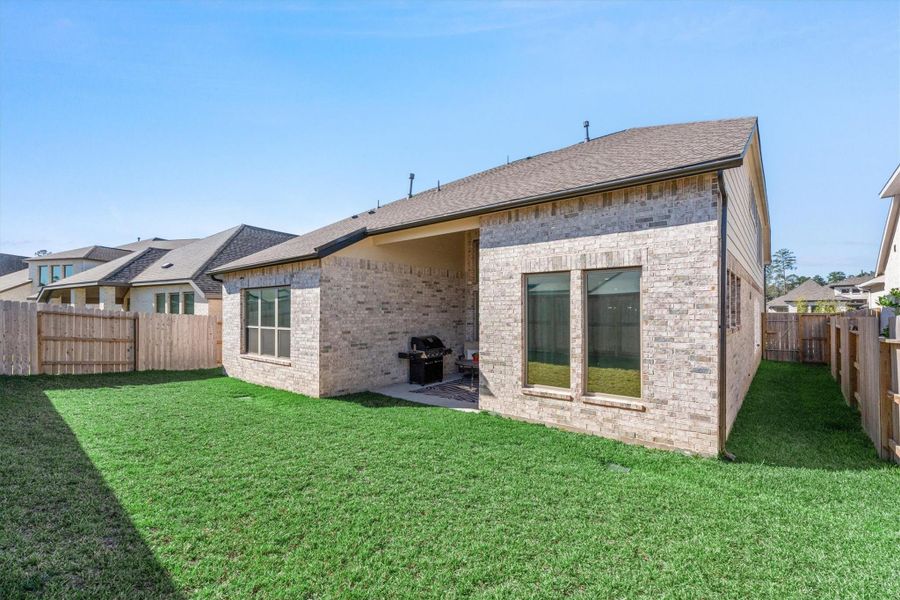 This photo shows the backyard of a home featuring a brick exterior, a covered patio, and a neatly fenced lawn, ideal for outdoor activities and relaxation.