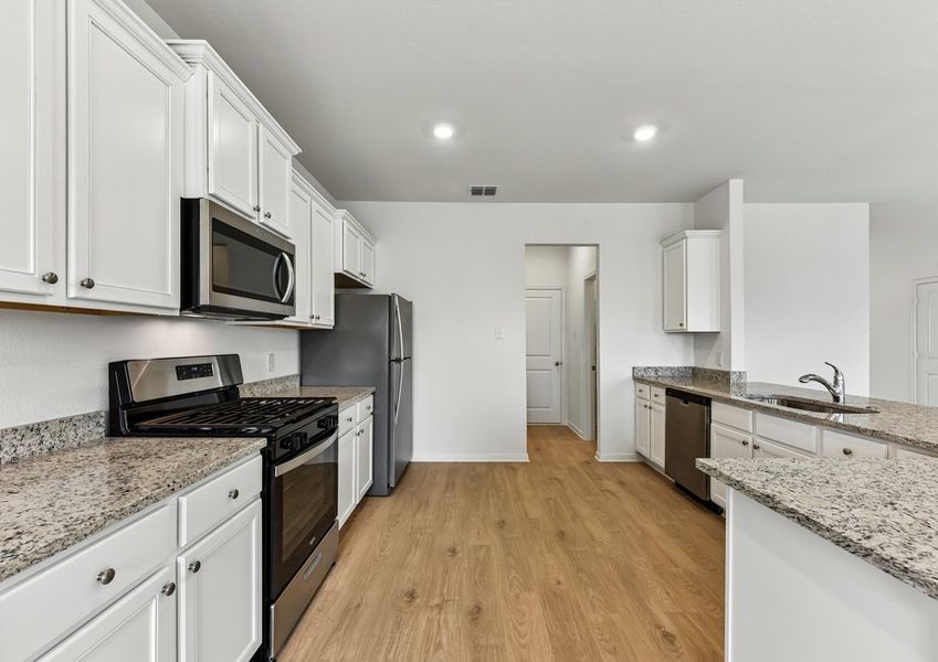 Kitchen featuring a stainless steel range, microwave, undermount sink, granite countertops, and white cabinetry.