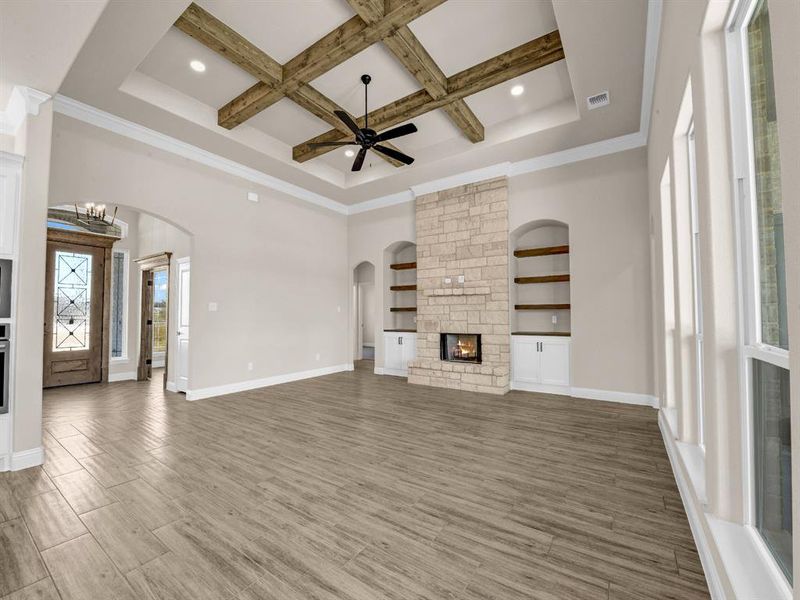 Unfurnished living room featuring a high ceiling, beam ceiling, ceiling fan with notable chandelier, a fireplace, and coffered ceiling