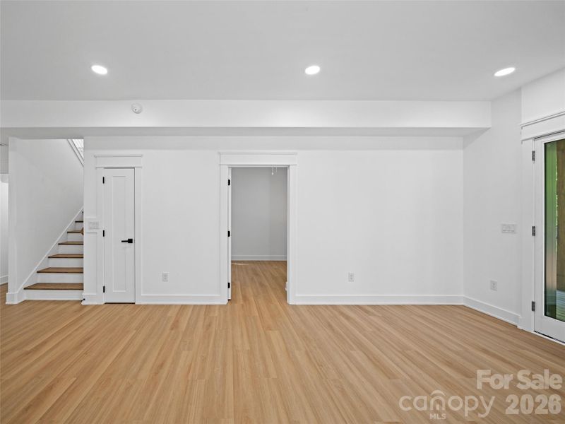 Great room in finished basement with bedroom door open exterior exit door and stairs to main level.