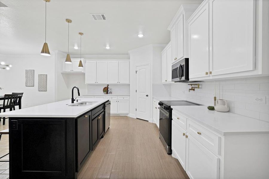 Kitchen with white cabinets, appliances with stainless steel finishes, a kitchen island with sink, and sink