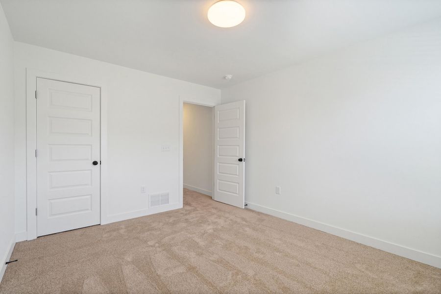 Carpeted room featuring white walls, white trim, and two white five-panel interior doors with black hardware Carpeted room featuring white walls, white trim, and two white five-panel interior doors with black hardware