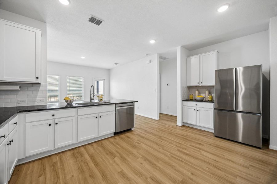 Kitchen with backsplash, stainless steel appliances, white cabinetry, light wood-style flooring, and dark stone countertops