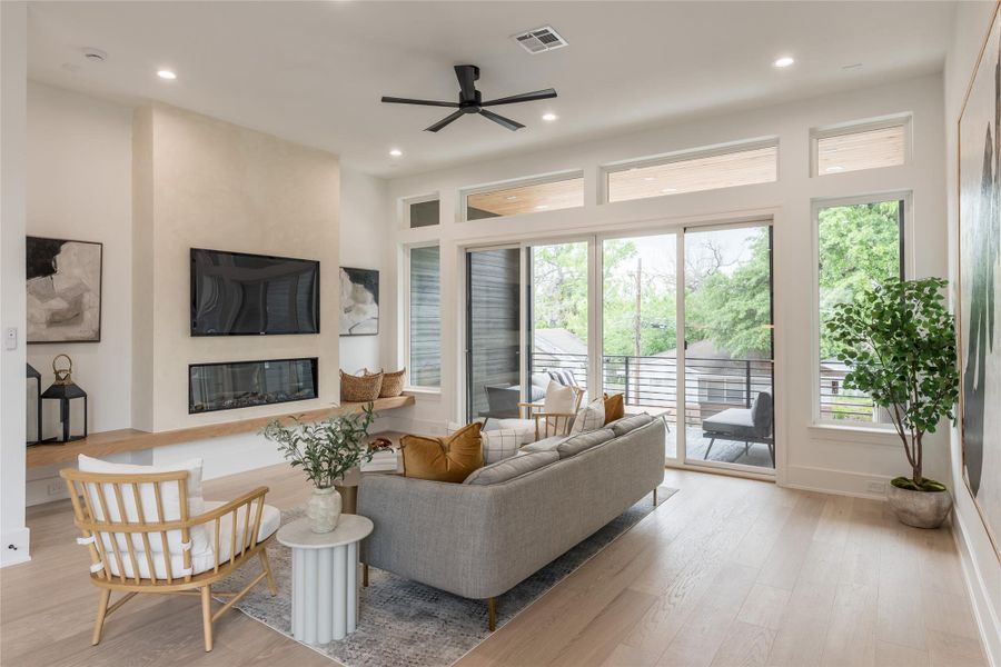 A living room that earns its light. Two walls of glass, recessed cans on dimmers, a matte-black five-blade fan, and a sculptural plaster fireplace wall that anchors the room without overwhelming it. Proof that restraint; in material, in palette, in line, is its own kind of luxury.
