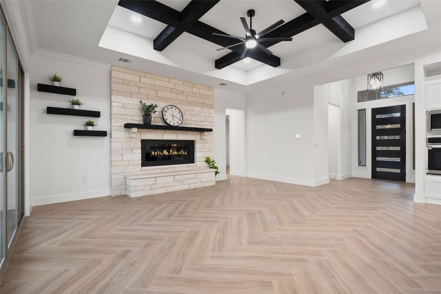 Unfurnished living room with coffered ceiling, a fireplace, a ceiling fan, and beamed ceiling