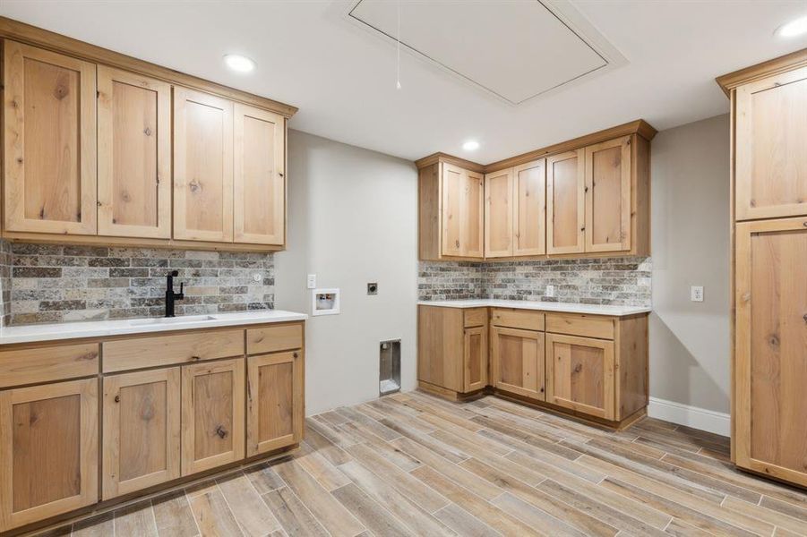 Laundry room with hookup for a washing machine/dryer, room for a second refrigerator, a sink, attic access, wood look tile floors, and cabinet space. Laundry room with hookup for a washing machine/dryer, room for a second refrigerator, a sink, attic access, wood look tile floors, and cabinet space.