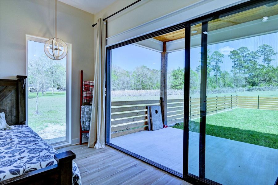 This photo showcases a cozy bedroom with large sliding glass doors opening to a covered patio and a lush, fenced backyard, offering serene views of surrounding trees and greenery.