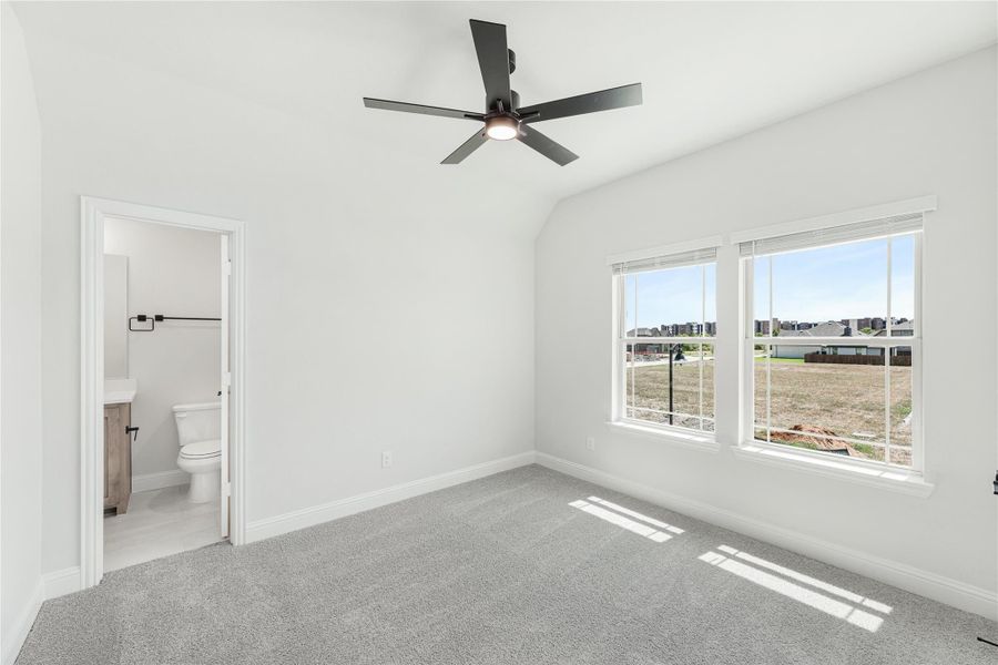 Bedroom with vaulted ceiling, ceiling fan, carpet floors, and ensuite bathroom access