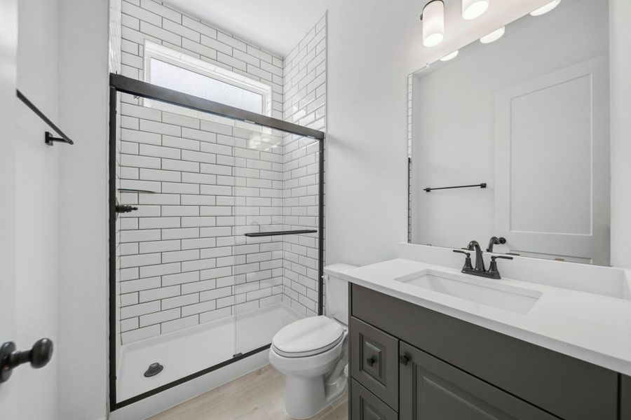 The downstairs full bathroom with a large walk-in shower, upgraded tile, and large vanity, is located just off the hall of the downstairs secondary bedroom, making it a perfect place for guests to unwind.