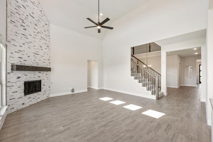 Open living room with vaulted ceiling, stone fireplace, ceiling fan, and staircase with metal balusters Open living room with vaulted ceiling, stone fireplace, ceiling fan, and staircase with metal balusters