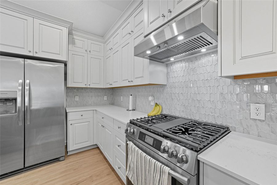 Modern kitchen with stainless steel appliances, white cabinetry, and a hexagonal tile backsplash. Modern kitchen with stainless steel appliances, white cabinetry, and a hexagonal tile backsplash.