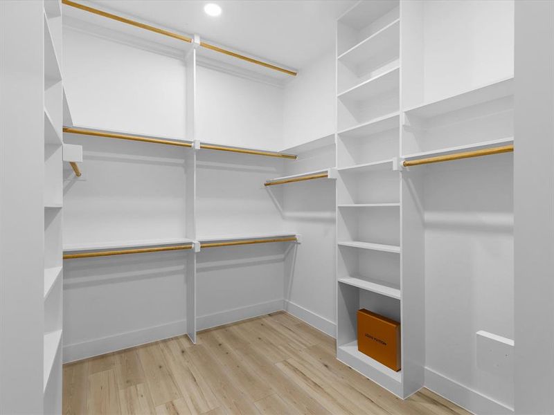 Custom closet system featuring wood-finish flooring, ample shelving, and multiple hanging rods
