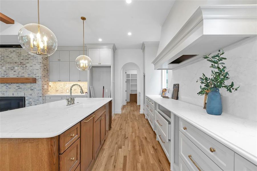 Two tone kitchen featuring two tone cabinets, light wood-type flooring, light stone countertops, arched walkways, and a kitchen island with sink
