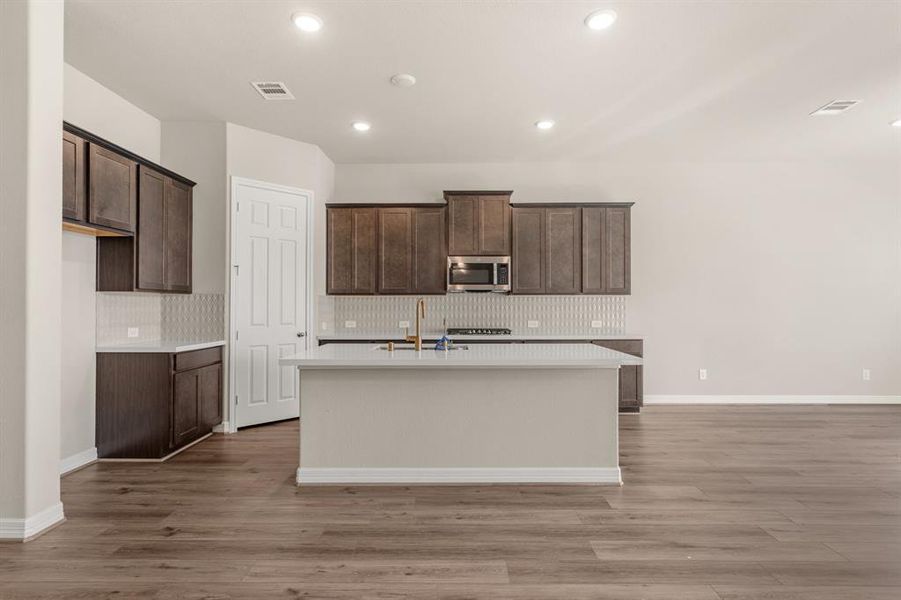 This light and bright kitchen features a large quartz island, dark stained cabinets, a large sink overlooking your family room, recessed lighting, and beautiful backsplash.