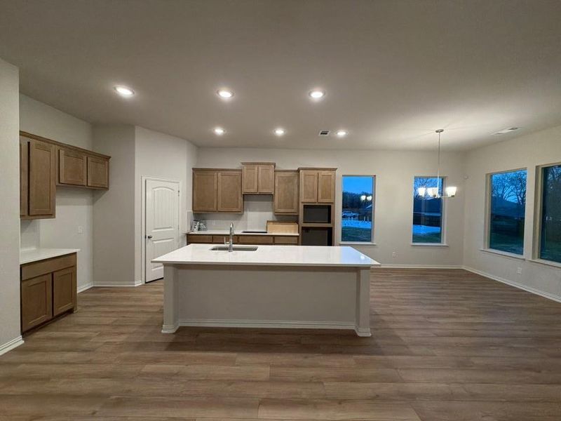 Kitchen with dark wood-style flooring, a chandelier, a kitchen island with sink, recessed lighting, and brown cabinets