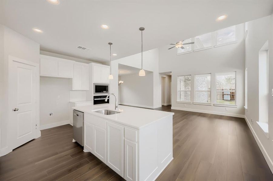 Open-concept living space featuring a central kitchen island with a stainless steel sink, white shaker cabinetry, and wood-finish flooring
