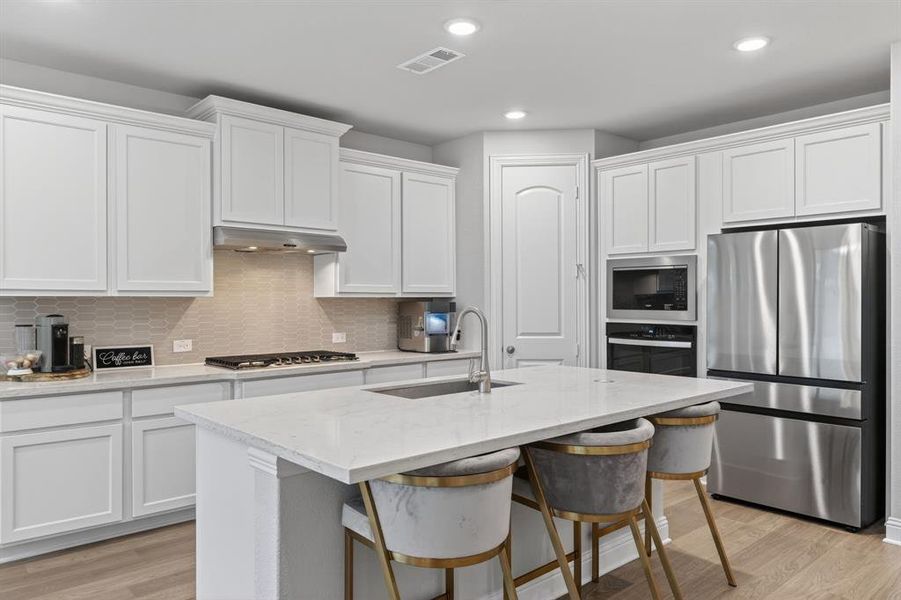 Kitchen featuring stainless steel appliances, white cabinetry, light stone countertops, a breakfast bar, and recessed lighting Kitchen featuring stainless steel appliances, white cabinetry, light stone countertops, a breakfast bar, and recessed lighting
