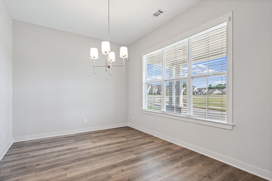 Bright interior space featuring wood-finish flooring, a large multi-pane window with horizontal blinds, and a contemporary chandelier