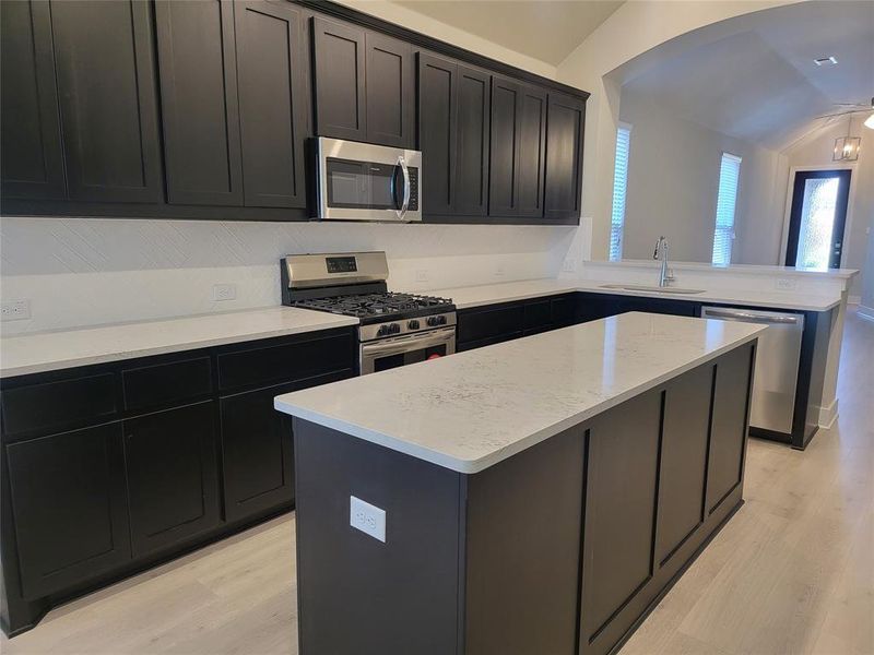 Kitchen featuring a sink, appliances with stainless steel finishes, a peninsula, light wood finished floors, and lofted ceiling